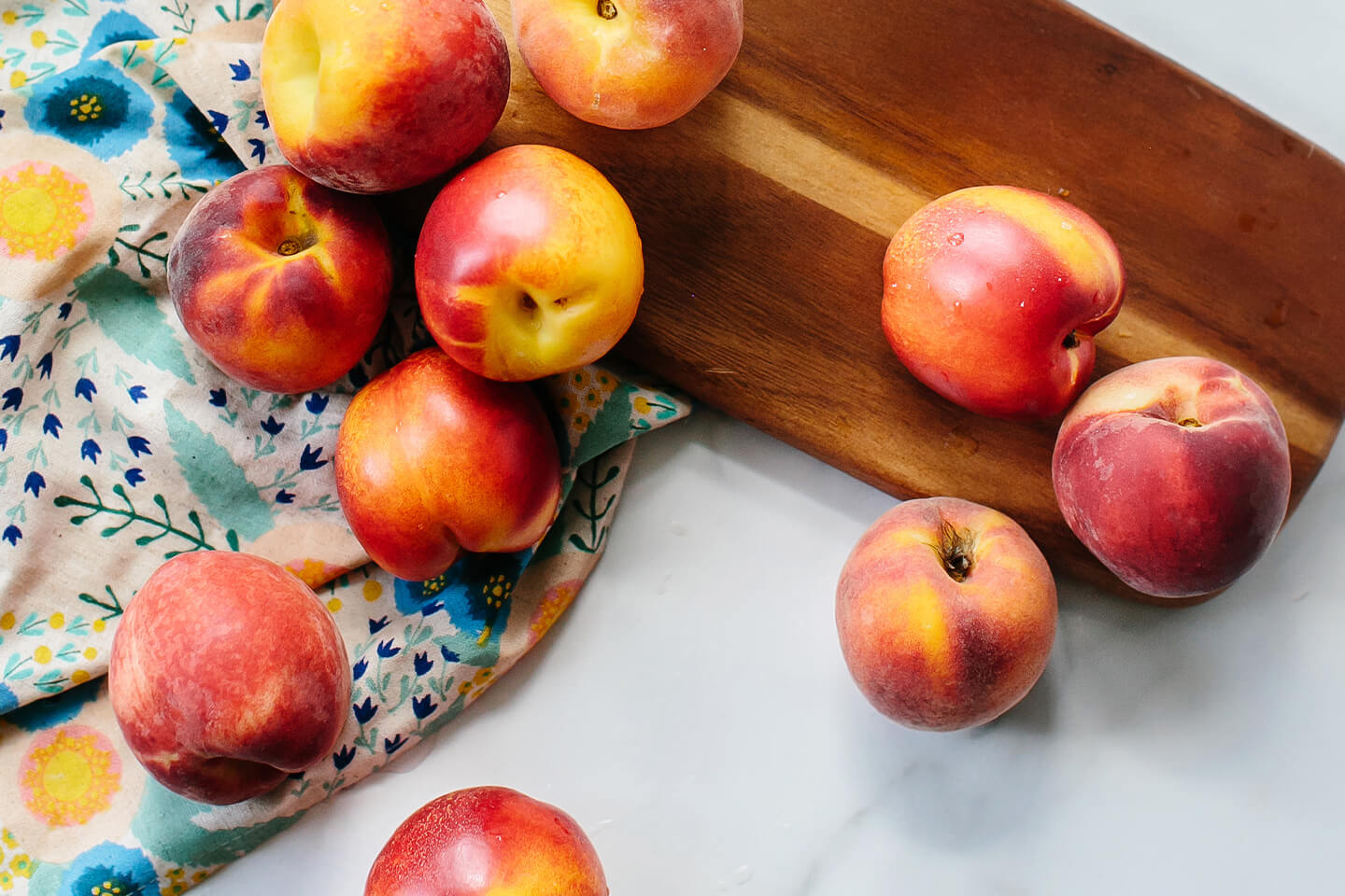 Ten whole peaches on a countertop next to a cutting board.