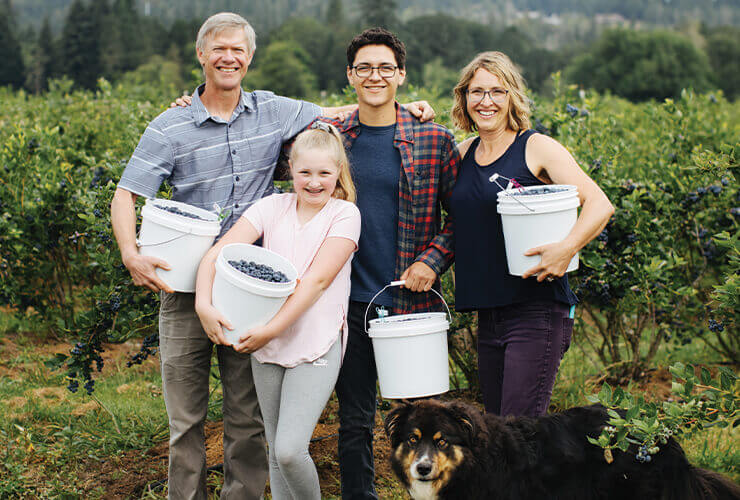 a family holding large white buckets full of fresh blueberries on a farm.