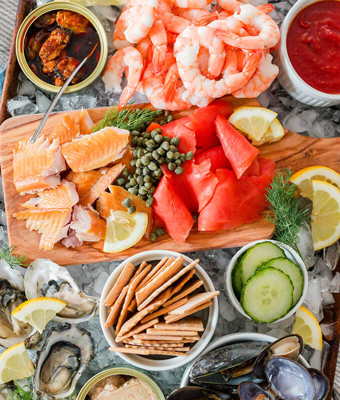 an overhead shot of a seafood board with shrimp, smoked fish, crackers, oysters, cucumbers, lemon and more!
