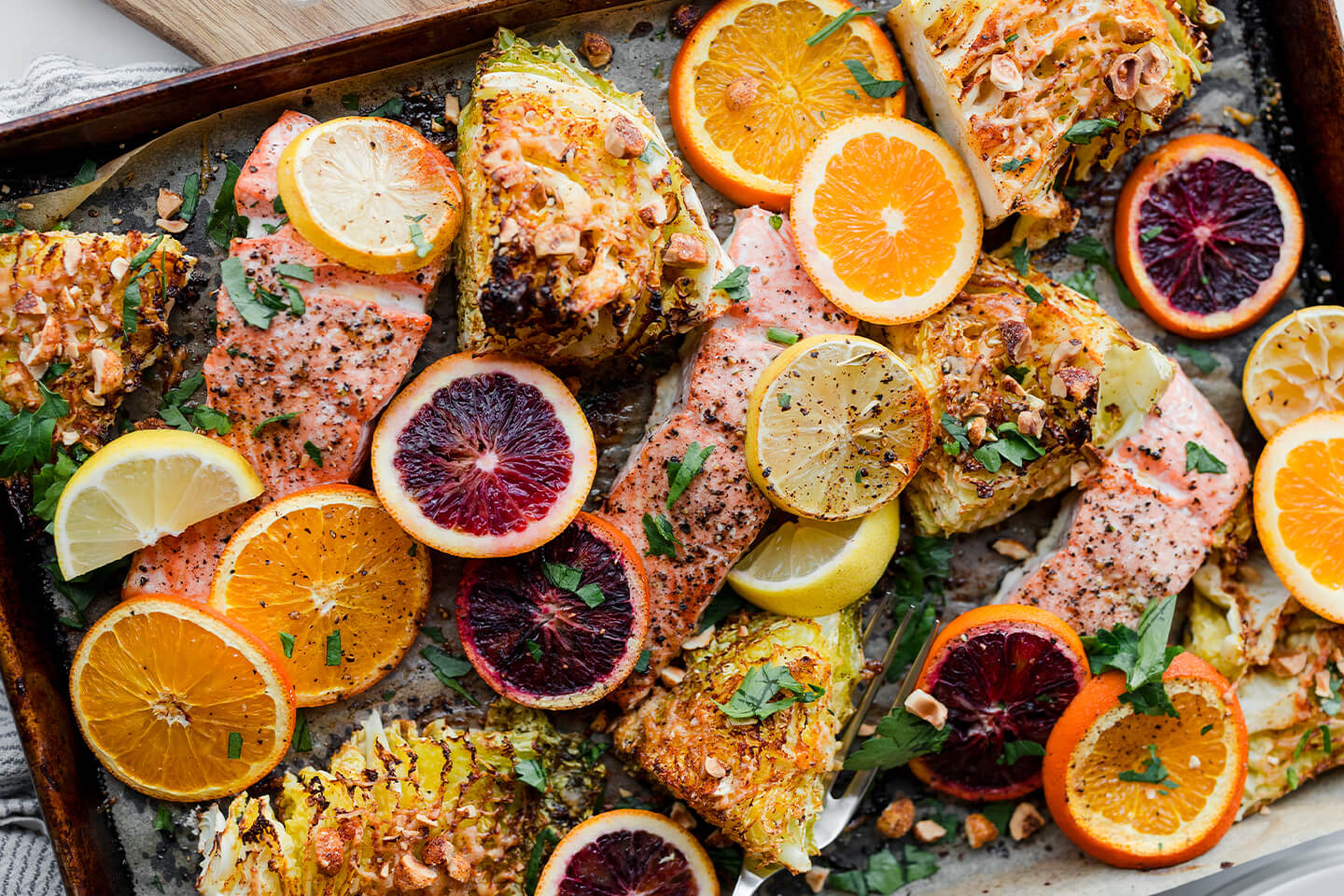 Roasted cabbage and salmon on a sheet pan with sliced citrus.