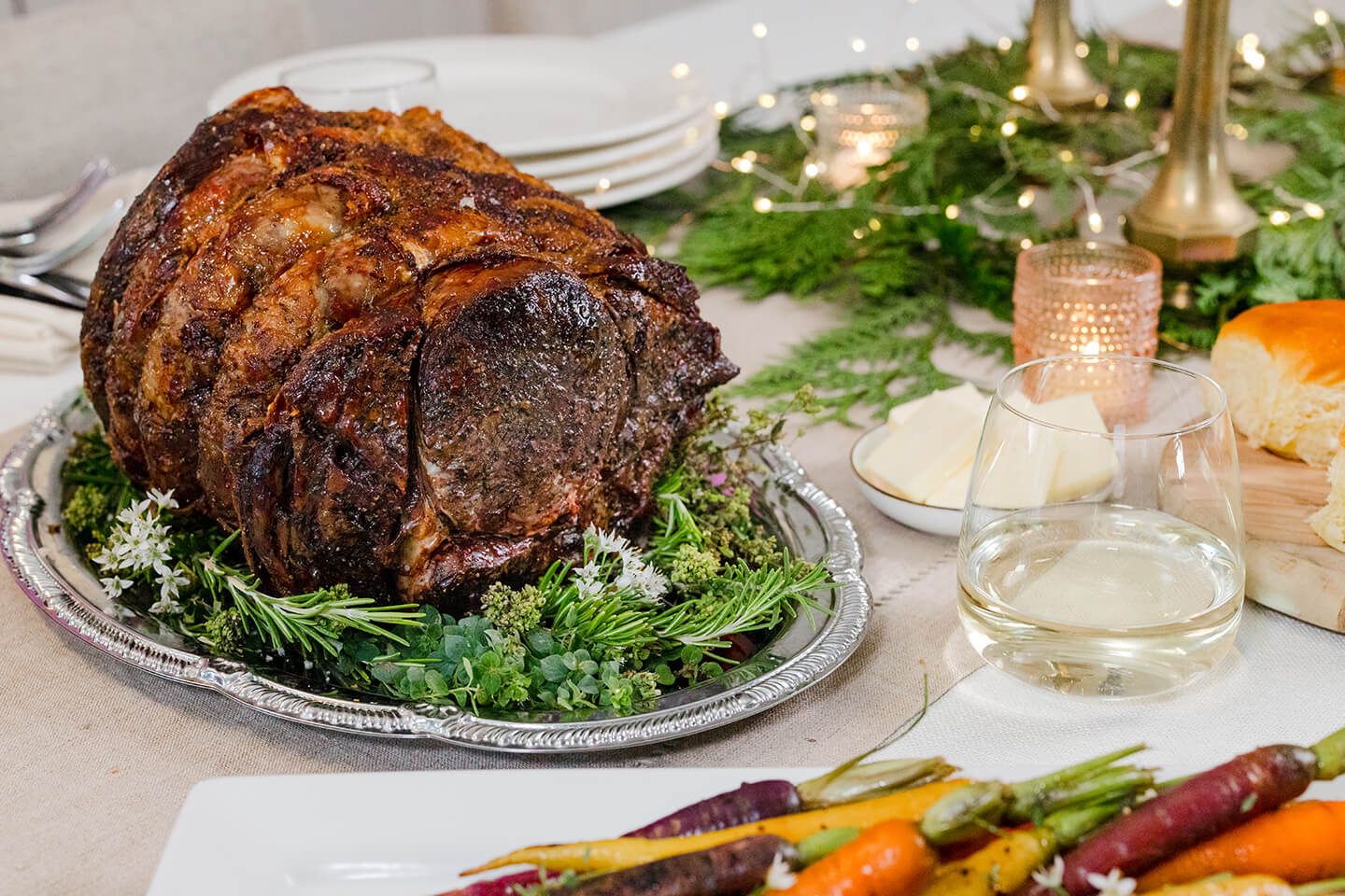 a holiday prime rib roast on a platter featured on a holiday table with carrots, wine and holiday decor.