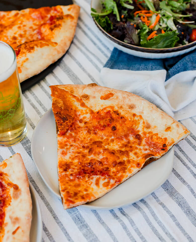 a fresh slice of pizza on a plate with a pint of beer and side salad