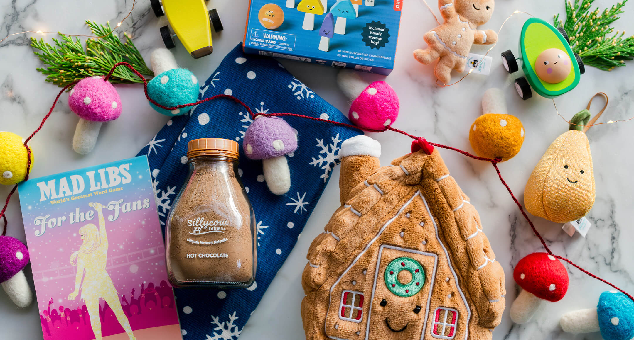 Toys and goodies for kids, including hot cocoa mix, a stuffed gingerbread house, and games.