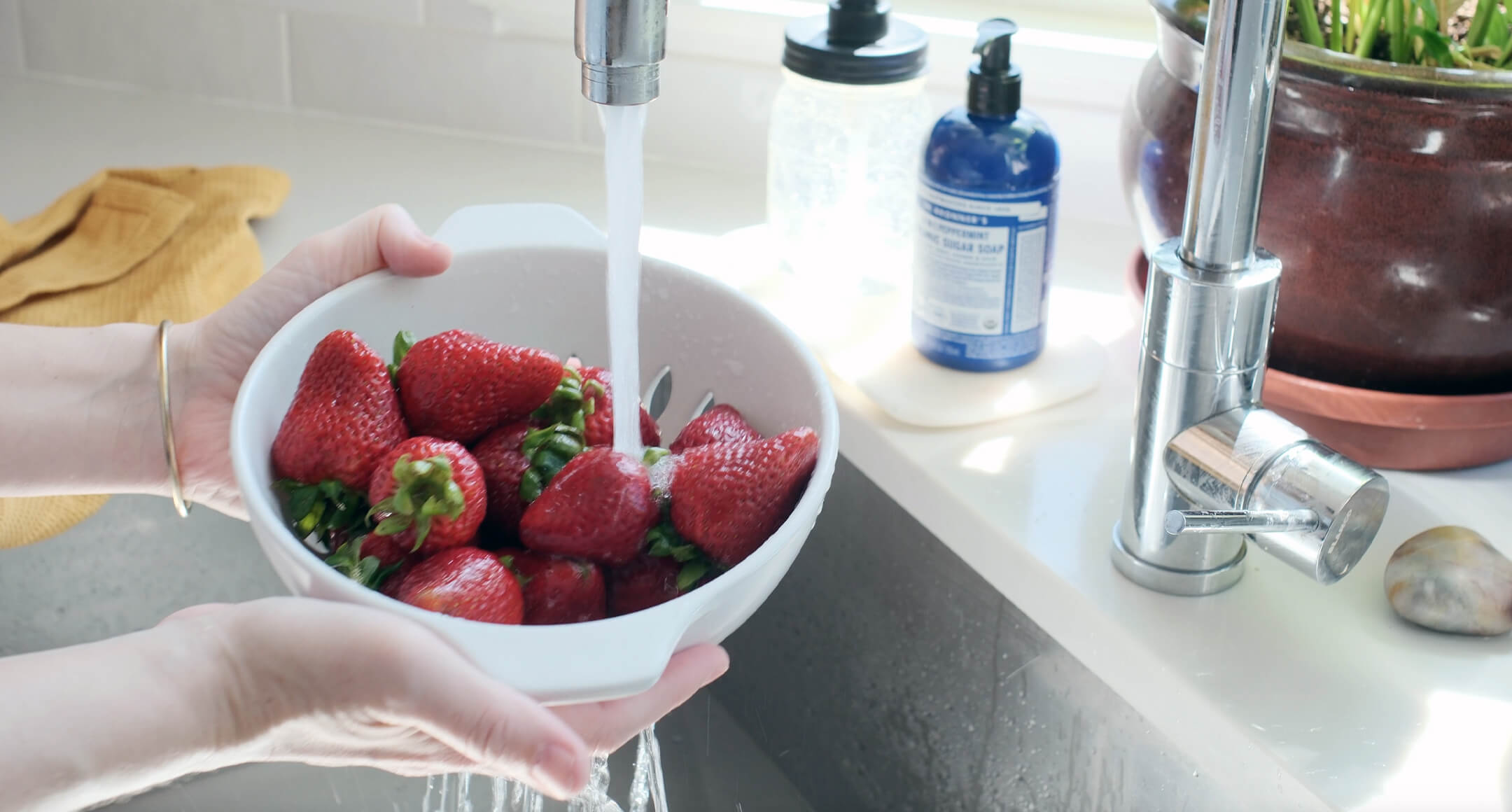 hands holding strawberries in a colander under running water