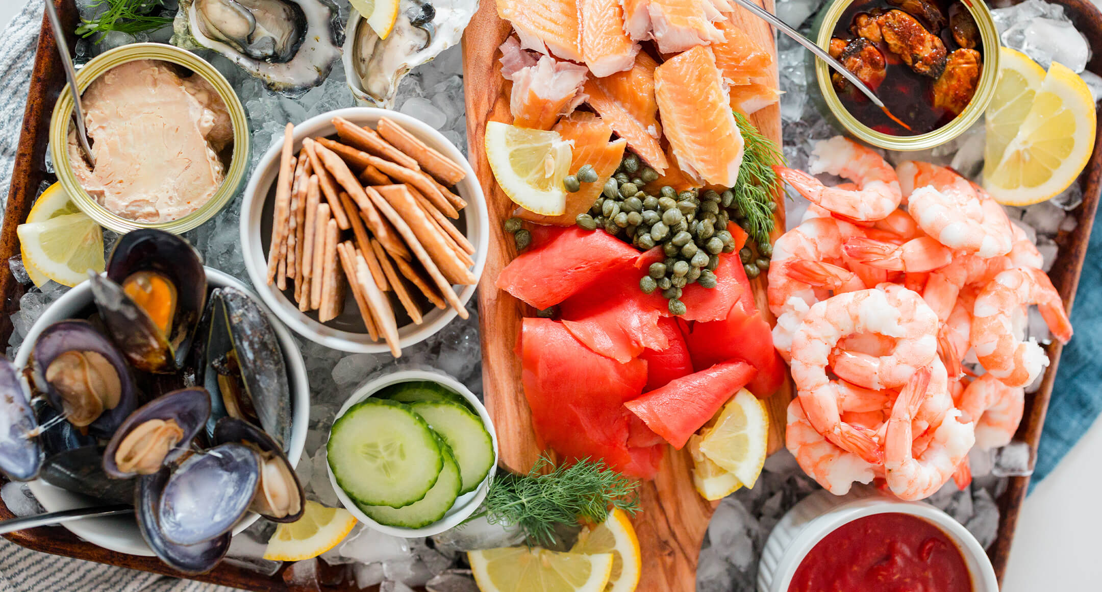 Cooked shrimp, smoked fish, oysters, and tinned fish arranged on a bed of ice.