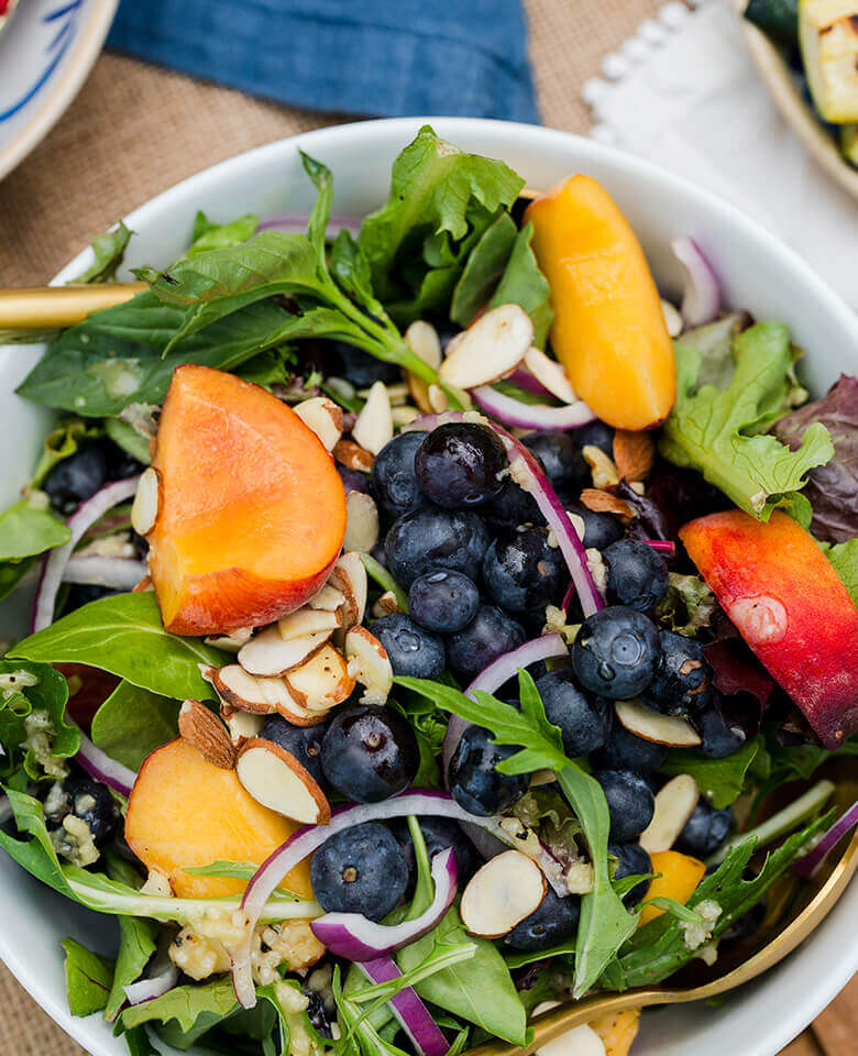 a photo of a peach and blueberry salad with fresh greens.