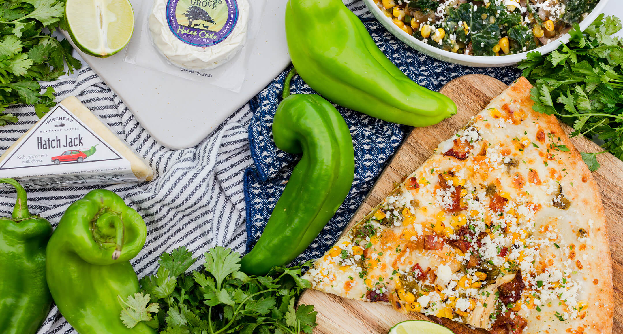 A variety of food items featuring seasonal Hatch chiles, including pizza, cheese, corn salad. 