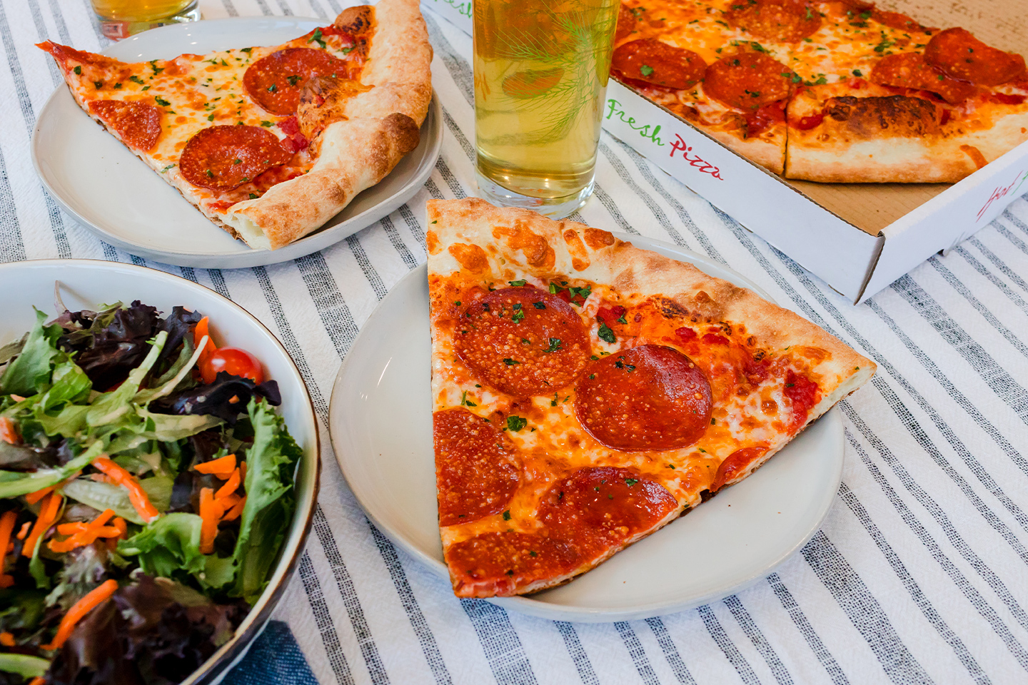 A slice of pepperoni pizza on a plate next to a side salad.