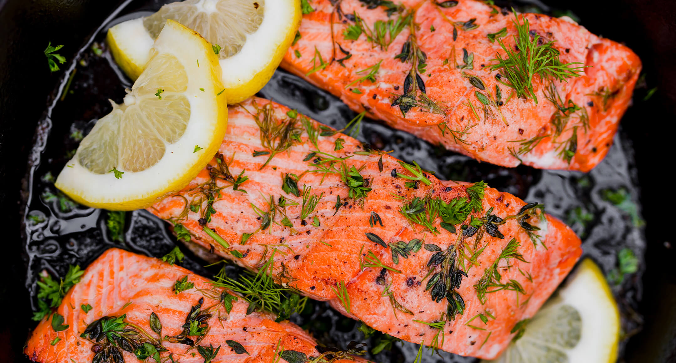 Salmon fillets in a pan with herbs and lemon slices.