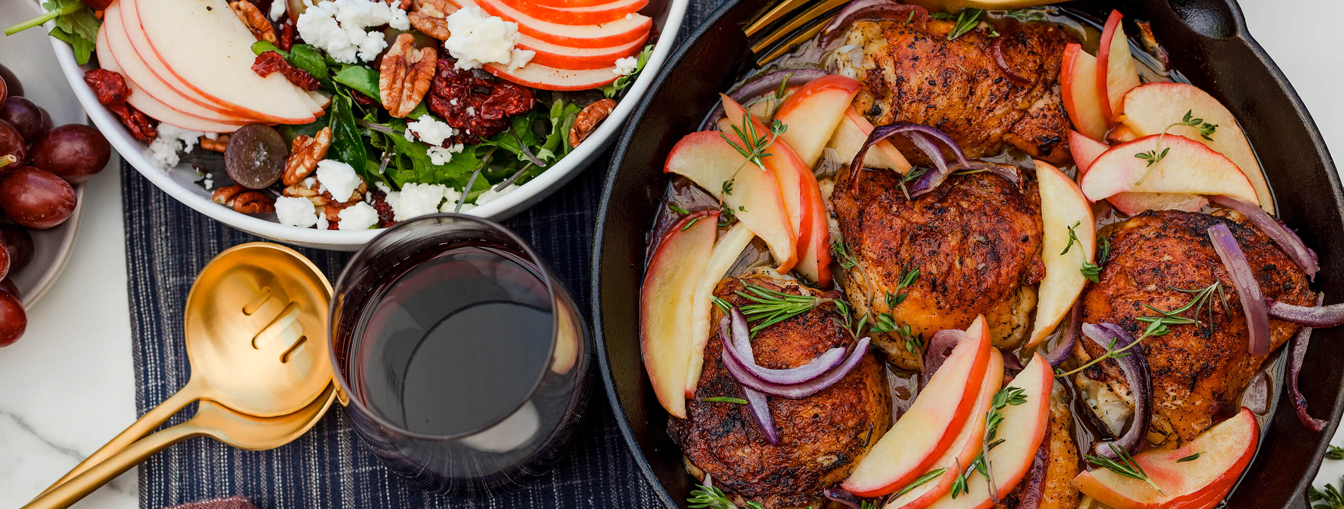 A cast-iron pan with roasted chicken thighs, sliced apples, and red onion. 