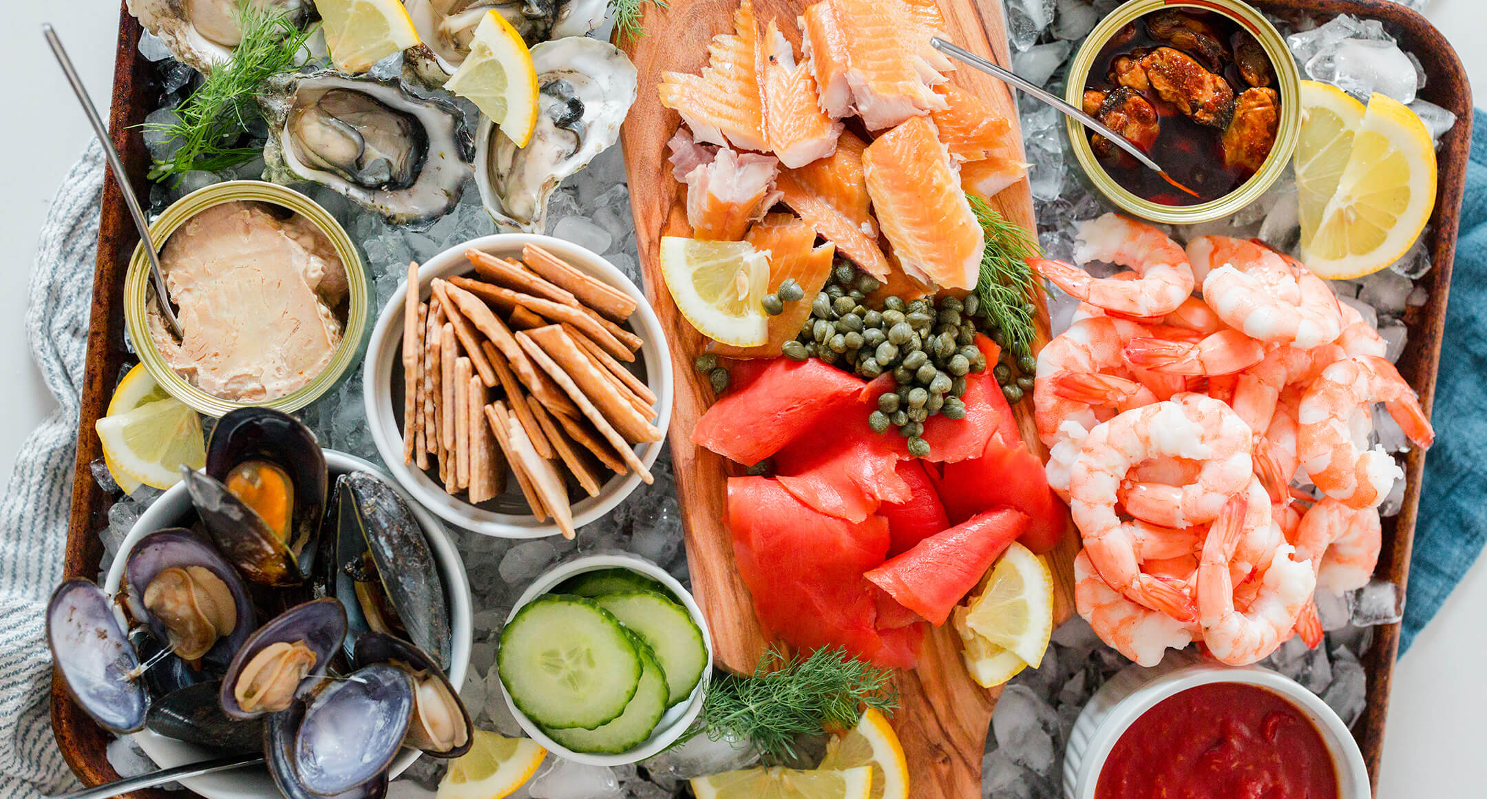 A sea-cuterie board featuring an array of sustainable seafood on ice, including tinned fish, shrimp, and smoked fish.