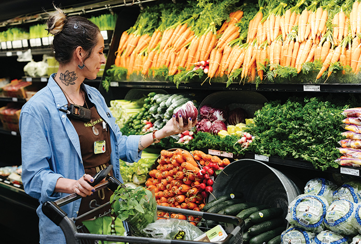 a staff member with their hair up in a bun, shopping the produce section full of carrots.