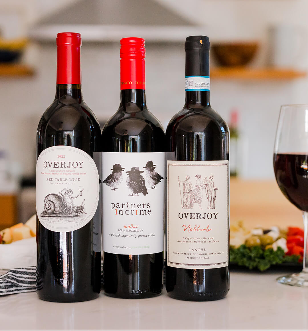 Three bottles of red wine on a tabletop from New Seasons wine partners Overjoy and Partners in Crime.