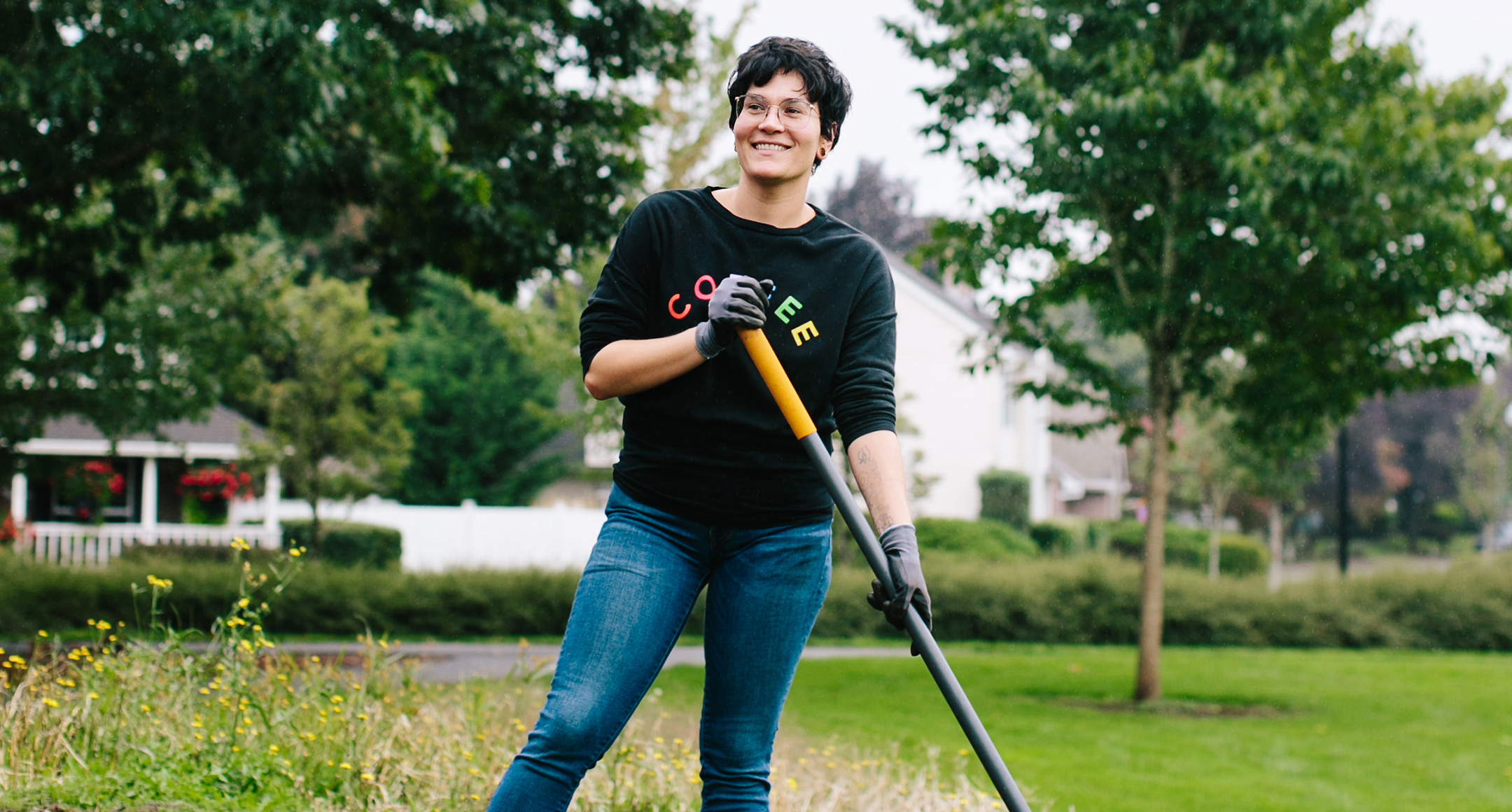 Staff member on a Lend a Hand activity holding a rake and wearing gardening gloves in a field.