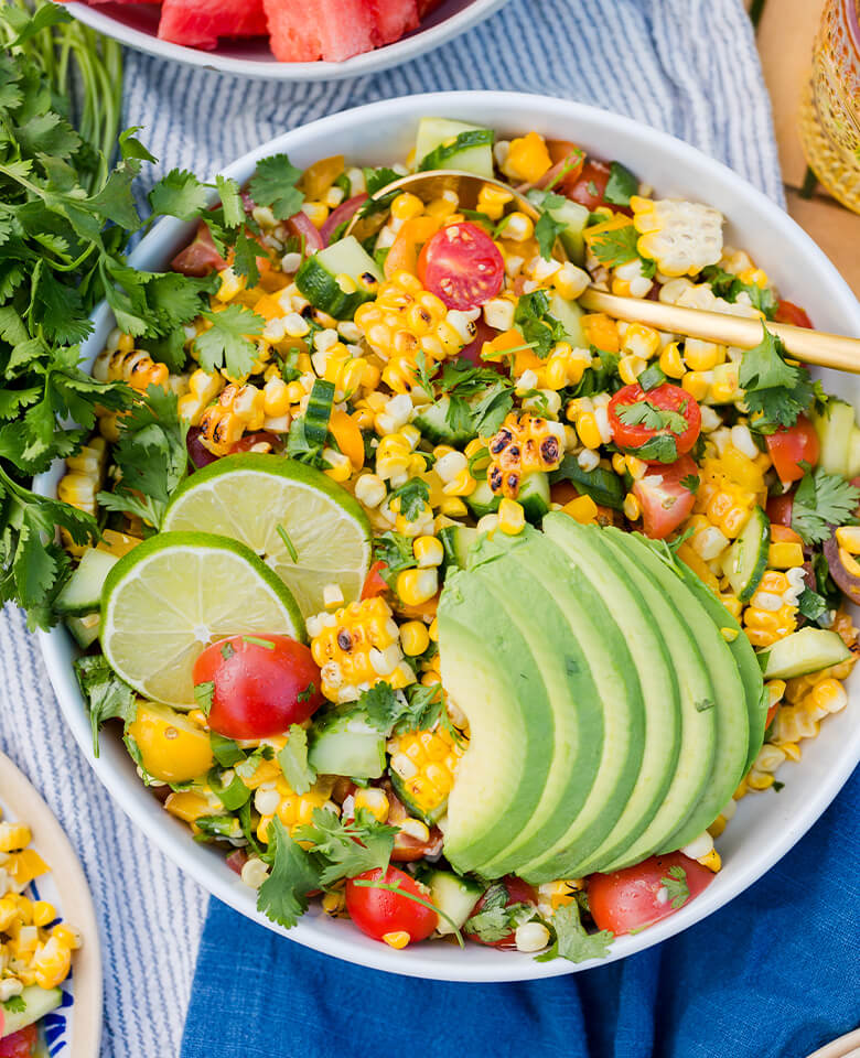 A bowl filled with corn salad garnished with cilantro, lime and avocado