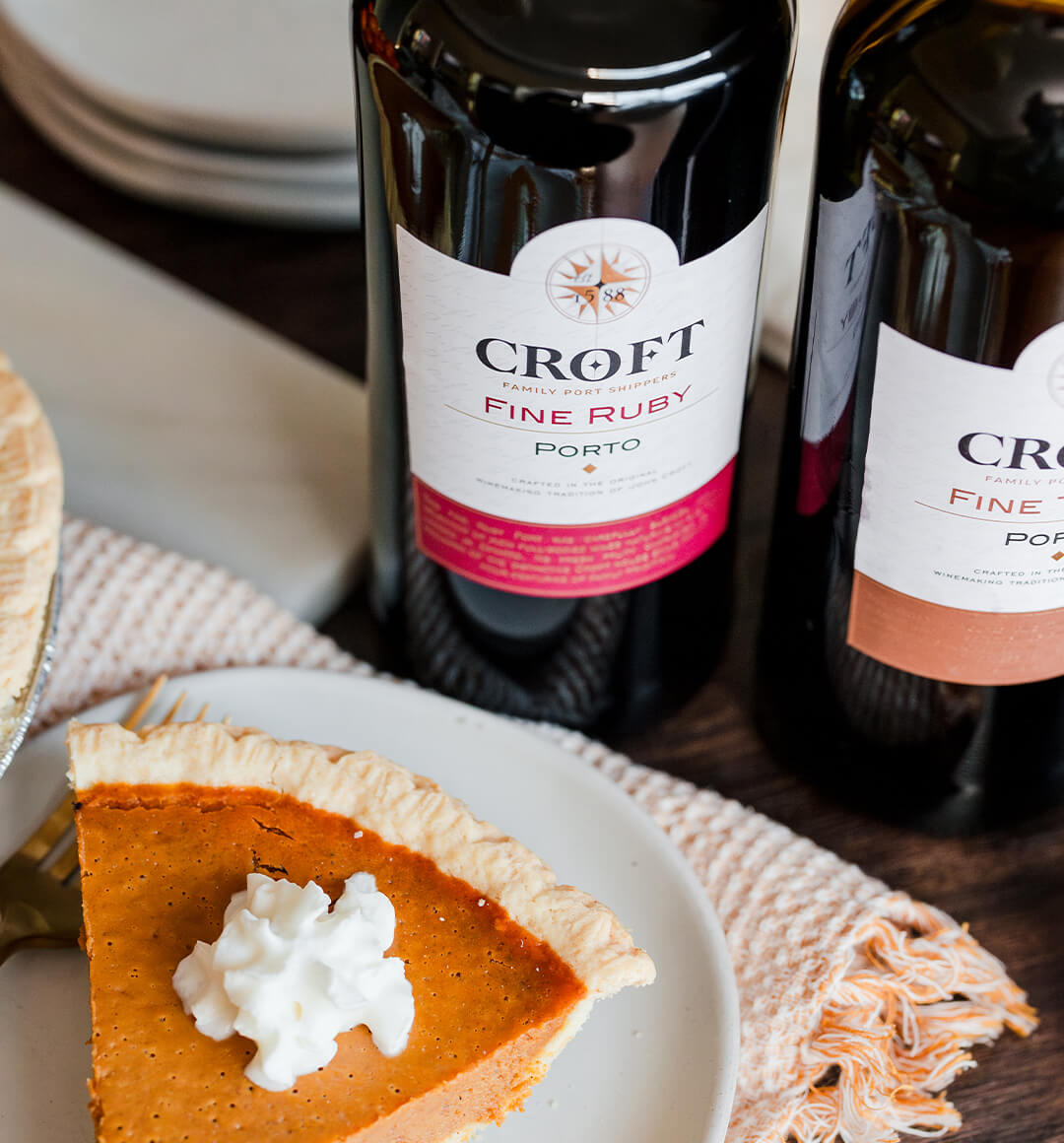 A slice of pumpkin pie next to two bottles of Croft Porto. 