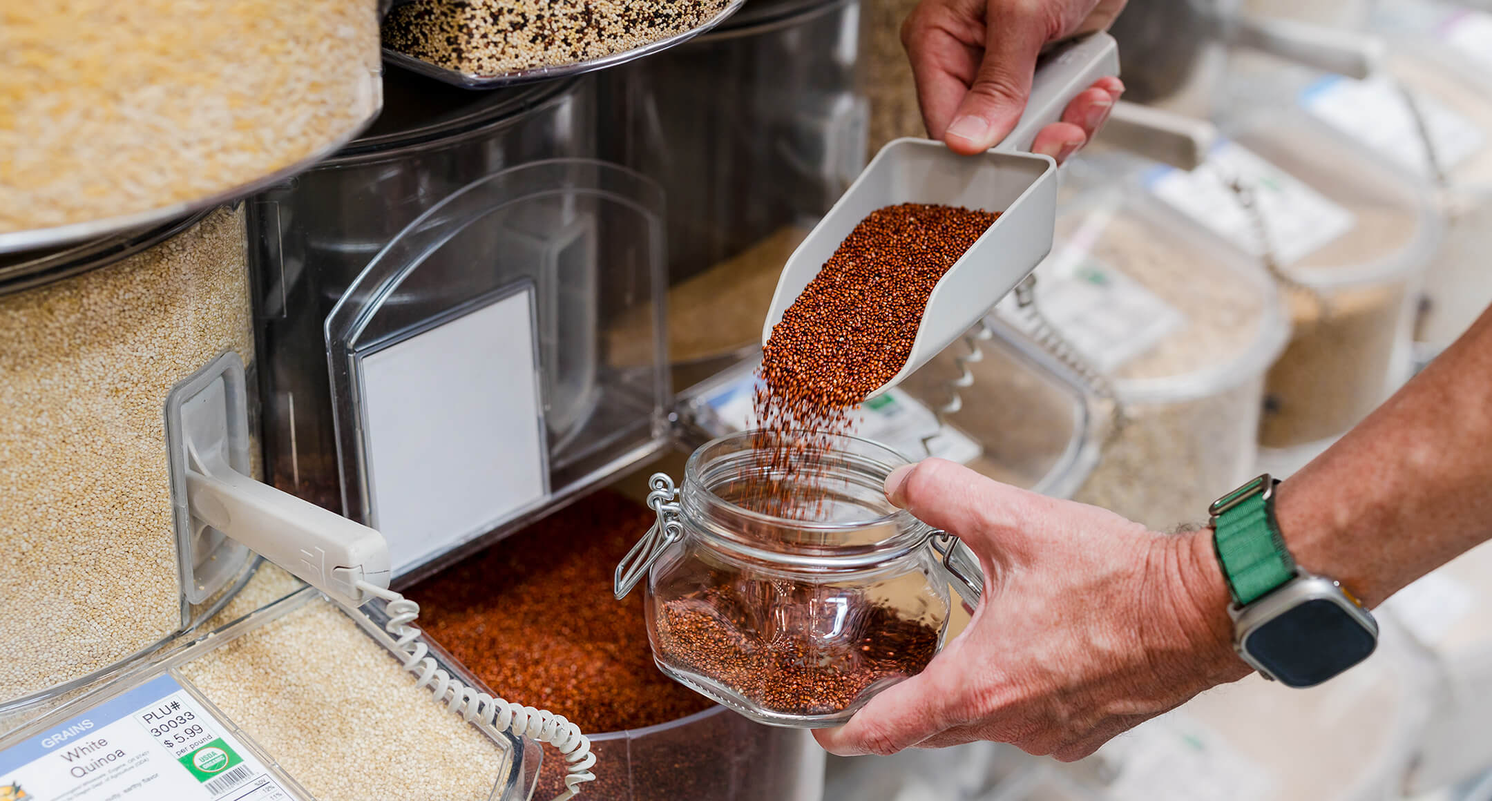 Hands scooping a bulk food item from the bin and into a reusable container at the grocery store. 