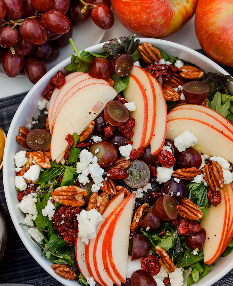 A fresh, fall salad in a bowl featuring apple, grapes, goat cheese, and dried cranberries.