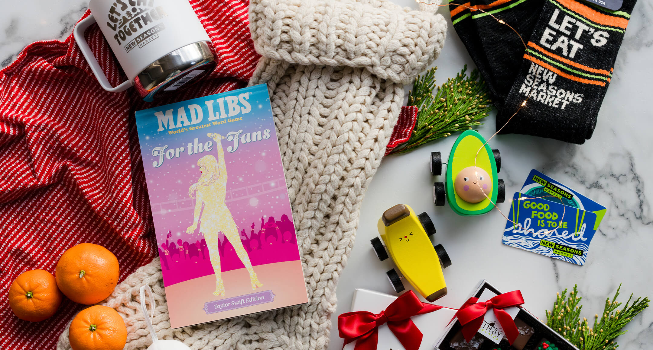 A knit stocking with the gifts to go inside next to it, including satsumas, socks, Mad Libs game, and food-related toys.