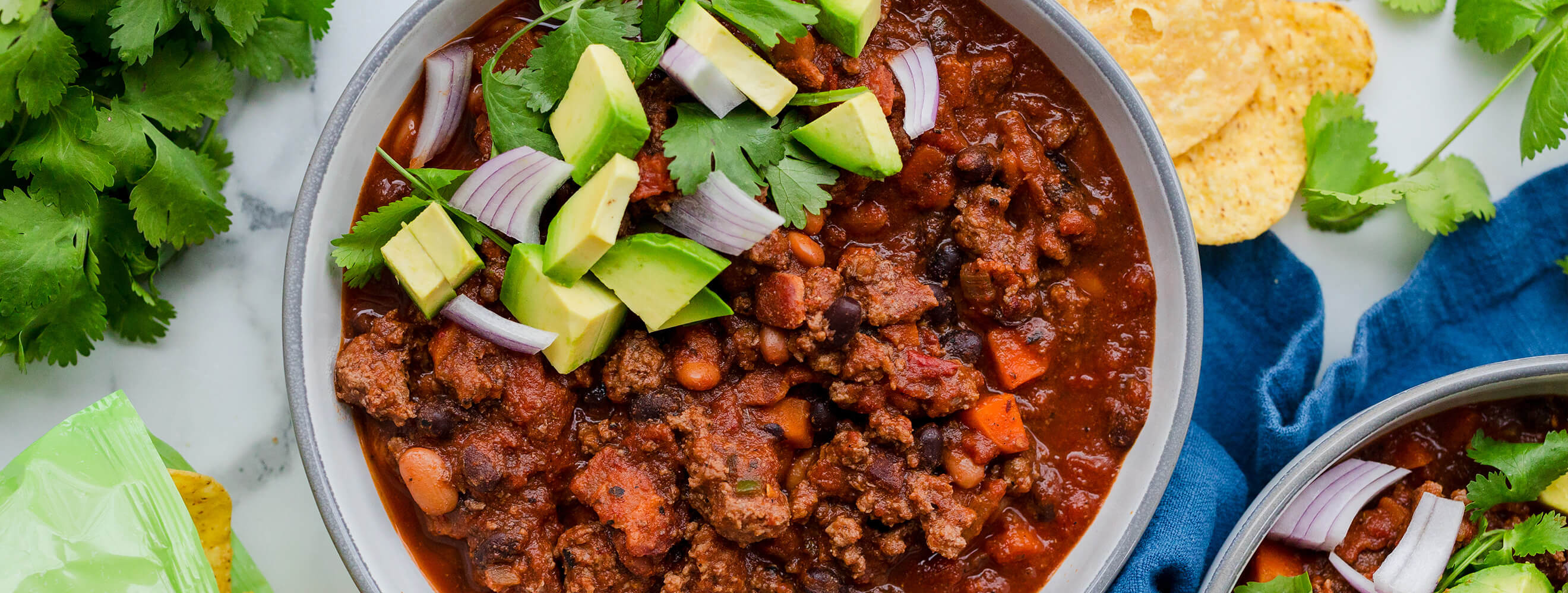 a white bowl with beef chili topped with fresh avocado and onions